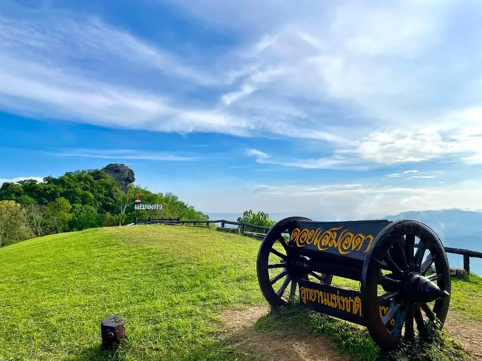 ป้ายดอยเสมอดาวบนแท่นไม้รูปทรงเกวียน พร้อมลานหญ้าสีเขียวและแนวภูเขา