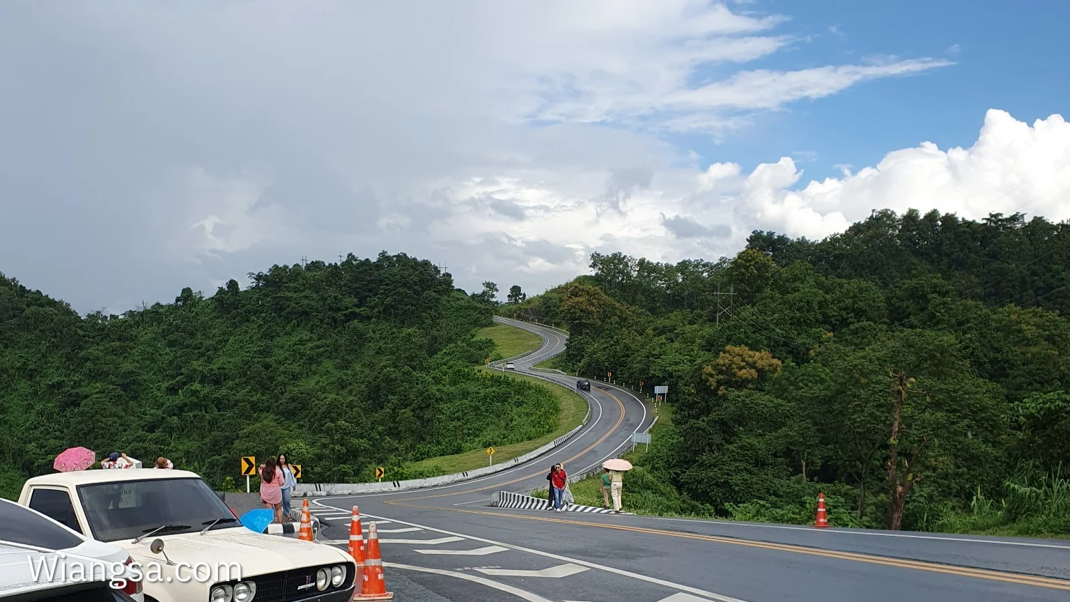 ภาพถ่ายถนนโค้งเลข 3 จังหวัดน่าน เห็นถนนคดเคี้ยวขึ้นสันเขา มีรถและจุดแวะถ่ายภาพด้านหน้า