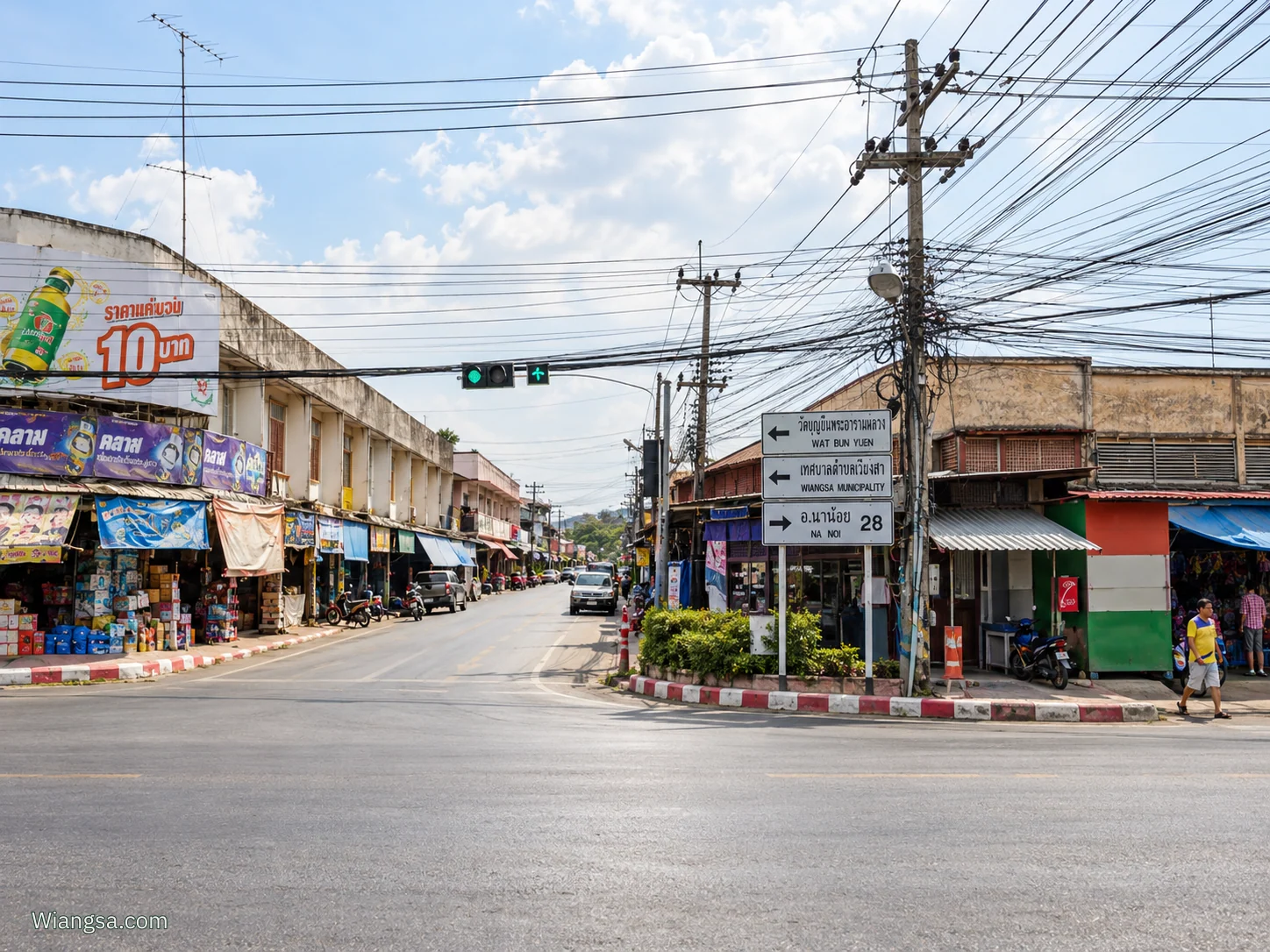 สี่แยกขี้นก เวียงสา มองเห็นสัญญาณไฟ ป้ายบอกทางวัดบุญยืนและนาน้อย ร้านค้าสองฝั่งถนน และตลาดเช้าที่หัวมุมขวา